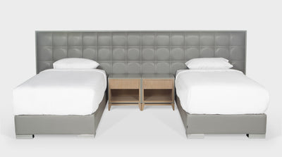 A bed set that has a grey leather, upholstered headboard, with a block stitch detail, and a timber frame. It also has two, grey leather, upholstered, single, bed bases that have steel legs, front view.