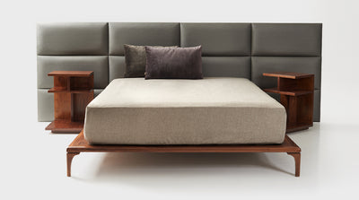 An upholstered, grey, panel headboard with a slim walnut bed base.