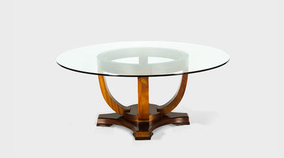 A luxury dining table inspired by art deco design. It has a natural mahogany base and sinuous curving legs with a round, clear, glass top.