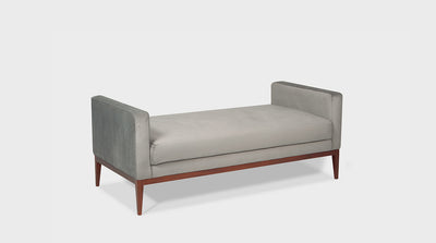A fully upholstered, grey ottoman with arms. It has medium mahogany, tapered legs. 