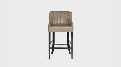 A mid-century inspired barstool that has a putty coloured, leather upholstered seat that is fluted and has a cross-stitching detail. It has dark mahogany legs. 