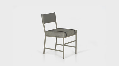 A contemporary dining chair that has a grey powder coated steel frame as well as grey upholstery on both the back rest and seat, which also features charcoal grey strap details with buckles. 