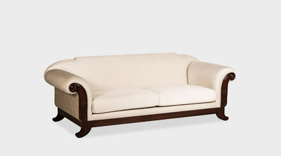 A classic sofa with luxury cream upholstery and ornate hand carvings of lotuses and scrolls on its mahogany frame.