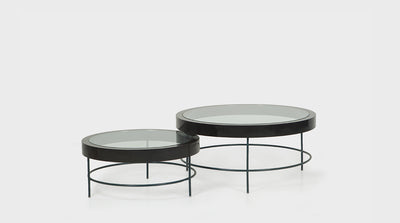 Round, modern, nesting coffee tables with glass tops, black, timber frames and slim, black, powder coated, steel legs with a round base. 