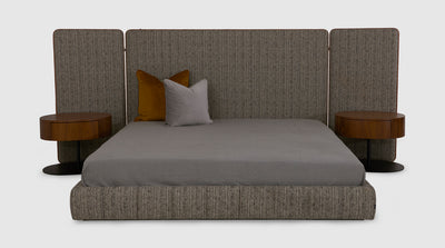 This contemporary bed has a tall, fully upholstered headboard with folding wings and burnt orange trim. It also has a low, fully upholstered, fluted, bed base. With walnut, oval, pedestals.