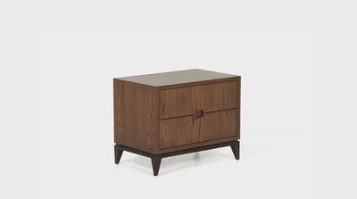 A mid-century inspired pedestal with two oak drawers that have groove handles and dark mahogany, tapered legs.