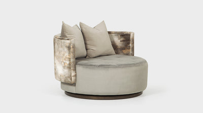 A modern barrel chair with a round design that swivels on its oak timber base. It is fully upholstered with two toned grey velvet fabrics and has a block stitching detail on its deep seat.