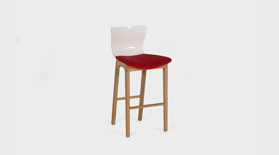 A barstool with an organic design and soft lines. It has a low, white backrest, curved, red, upholstered seat and oak legs. 