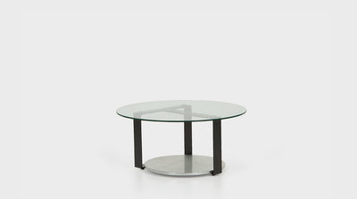 A contemporary coffee table with a round, glass top, black, powder coated, steel legs and a round, silver leaf base.