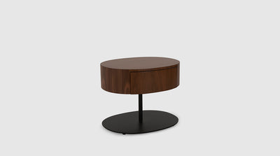 A retro inspired, walnut pedestal with an oval top that features one drawer, and has an oval, black, steel base.