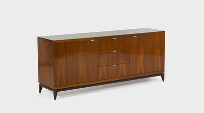 A mid-century inspired sideboard with walnut cupboards and drawers that have slim, steel handles. It has mahogany, tapered legs and a shadow line detail. 