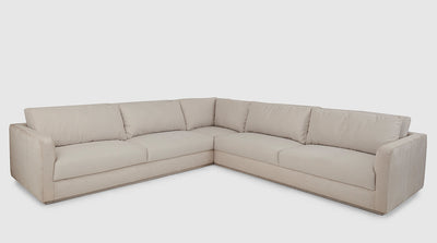 An off-white, fully upholstered corner sofa, with slouchy cushions and a slim oak base. 