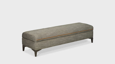 A fully upholstered grey contemporary ottoman with white double needle stitching, orange piping and oak legs.