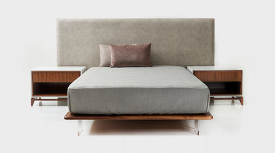 A modern minimalistic bed set with a fully upholstered, oatmeal coloured, headboard and walnut bed base featuring perspex legs.