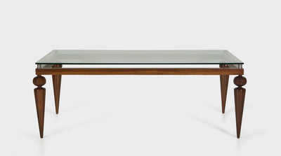A dining table that has a glass top, silver accents and a walnut base with tapered legs and round handcrafted details.