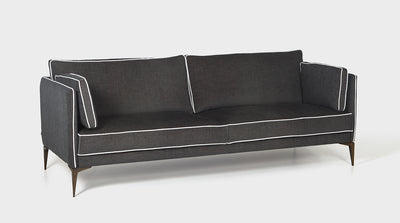 The Tuxedo sofa has a contemporary retro design with slim arms and chic oak legs. A fully upholstered charcoal grey luxury sofa with a white piping detail.